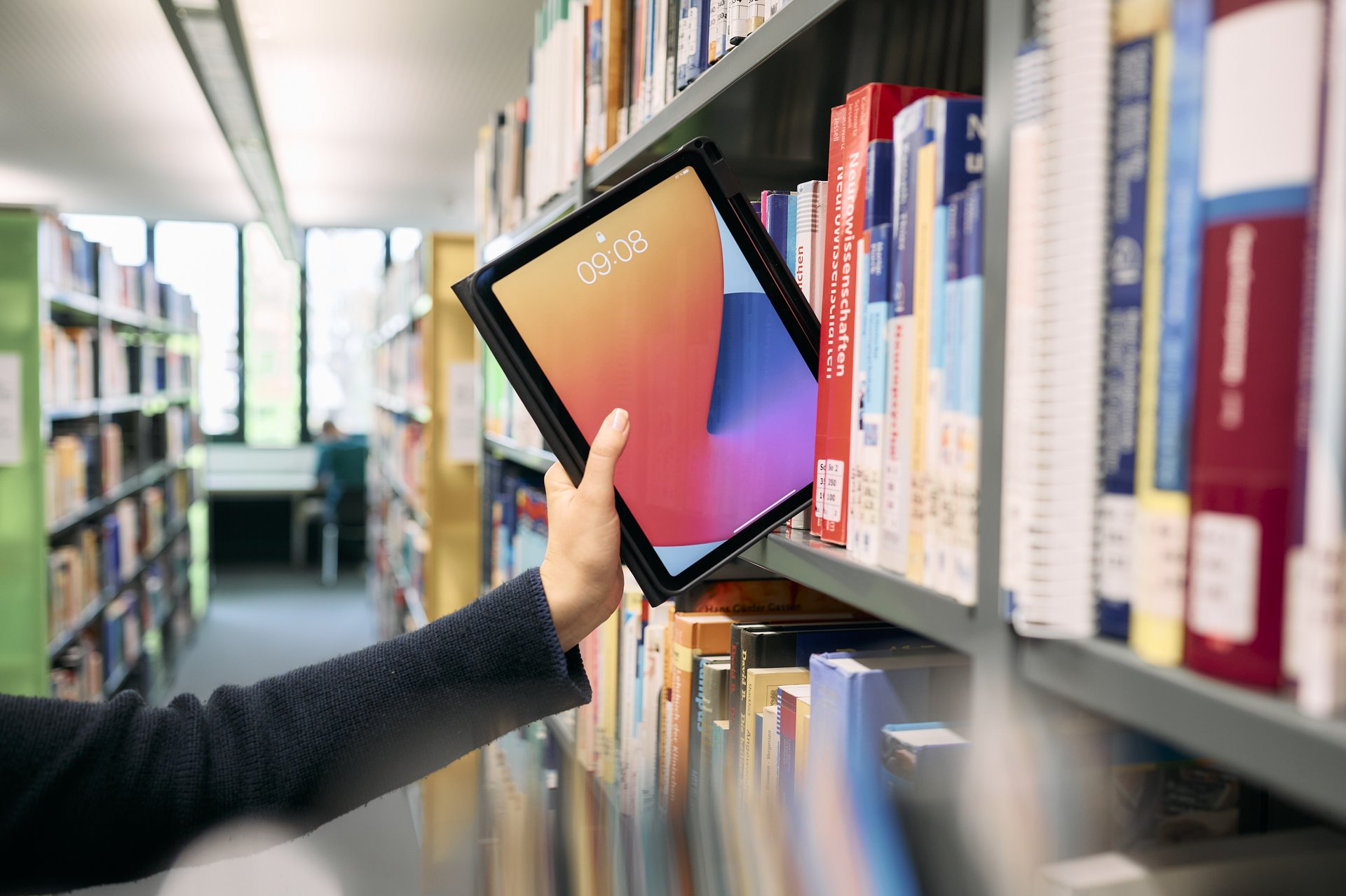 Tablet wird aus Bücherregal herausgeholt